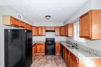Kitchen featuring black appliances, light stone counters, brown cabinetry, and under cabinet range hood
