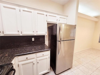 Kitchen with freestanding refrigerator, black range with electric cooktop, white cabinetry, light tile patterned flooring, and dark stone countertops