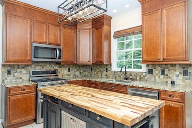 Kitchen featuring butcher block counters, decorative backsplash, stainless steel appliances, brown cabinetry, and decorative light fixtures