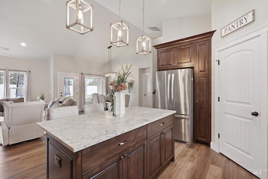 Kitchen with freestanding refrigerator, light wood-style floors, lofted ceiling, open floor plan, and hanging light fixtures