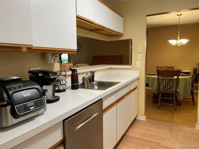 Kitchen with light countertops, white cabinetry, light wood finished floors, stainless steel dishwasher, and pendant lighting