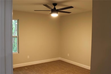 Spare room featuring dark carpet, a ceiling fan, and baseboards