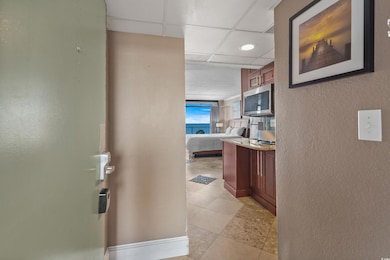 Corridor featuring a drop ceiling, a textured wall, and light tile patterned flooring
