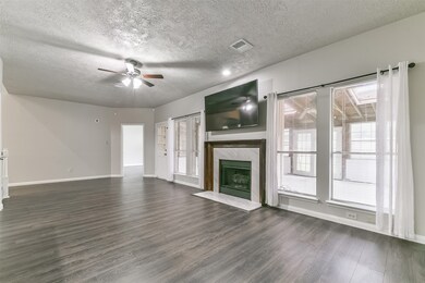 The rear wall of the family room is anchored by a gas log fireplace with a stylish tile surround and a milled wood mantle, flanked by a wall of windows dressed with blinds and sheer draperies. An enclosed porch lies just beyond.