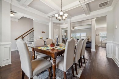 Dining space featuring coffered ceiling, dark wood-style floors, decorative columns, beam ceiling, and a chandelier