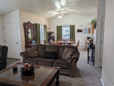Carpeted living area with vaulted ceiling, a ceiling fan, and a textured ceiling
