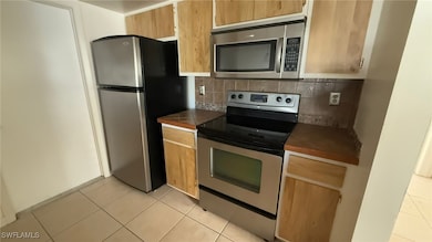 Kitchen with decorative backsplash, light tile patterned floors, and appliances with stainless steel finishes
