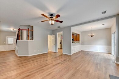 Unfurnished living room with a decorative wall, wainscoting, plenty of natural light, a chandelier, and light wood finished floors