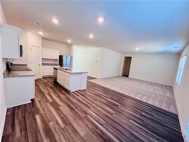 Kitchen featuring a center island with sink, stainless steel appliances, light stone countertops, dark hardwood / wood-style flooring, and white cabinetry