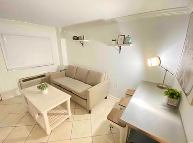 Living area with light tile patterned flooring, a wall mounted air conditioner, and baseboards