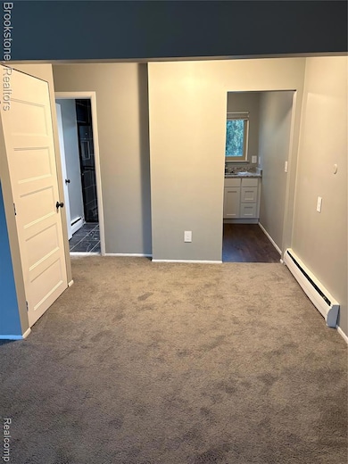 Unfurnished bedroom with connected bathroom, a baseboard radiator, and dark carpet