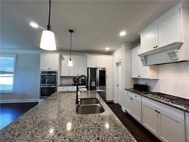 Kitchen featuring under cabinet range hood, appliances with stainless steel finishes, a sink, ornamental molding, and white cabinets