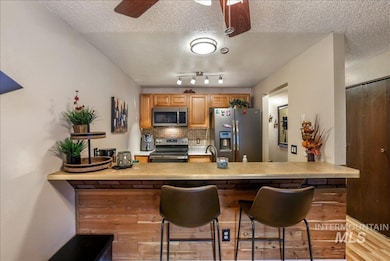 Kitchen with decorative backsplash, stainless steel appliances, a kitchen bar, a textured ceiling, and brown cabinets