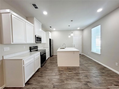 Kitchen with pendant lighting, white cabinets, sink, an island with sink, and stainless steel appliances