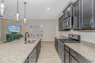 Kitchen featuring appliances with stainless steel finishes, a sink, baseboards, light wood finished floors, and light stone countertops
