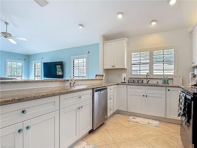 Kitchen featuring stainless steel dishwasher, range with electric cooktop, a ceiling fan, stone countertops, and white cabinets