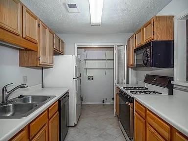 Kitchen with black appliances, a sink, light countertops, a textured ceiling, and brown cabinets