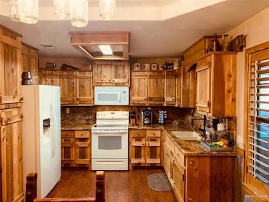 Kitchen with white appliances, dark wood-type flooring, brown cabinets, dark stone counters, and backsplash