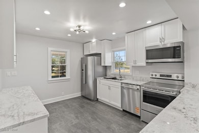 Kitchen featuring stainless steel appliances, white cabinets, recessed lighting, and light stone counters