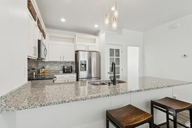 Kitchen featuring a peninsula, white cabinetry, appliances with stainless steel finishes, tasteful backsplash, and light stone counters