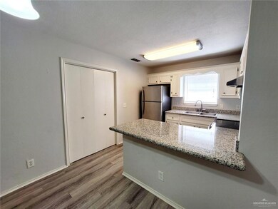 Kitchen featuring freestanding refrigerator, a peninsula, under cabinet range hood, wood finished floors, and light stone counters