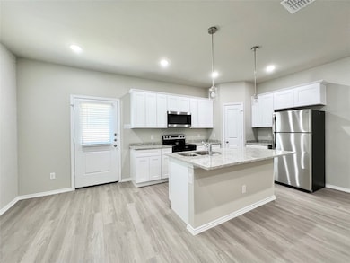 Kitchen featuring appliances with stainless steel finishes, pendant lighting, white cabinetry, light wood-style flooring, and light stone countertops