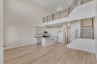 Kitchen with open floor plan, a towering ceiling, white cabinets, light wood-style floors, and a kitchen island with sink