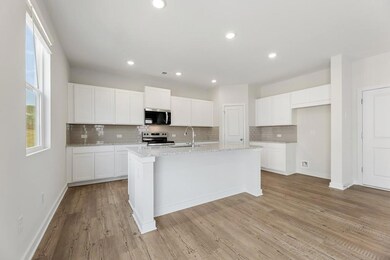 Kitchen featuring appliances with stainless steel finishes, backsplash, a kitchen island with sink, white cabinetry, and light wood finished floors