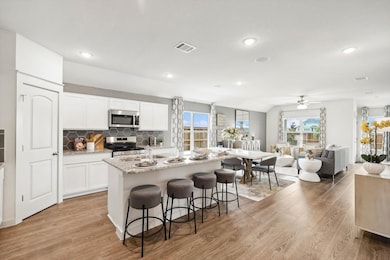 Kitchen featuring tasteful backsplash, open floor plan, a kitchen island with sink, white cabinets, and light stone countertops