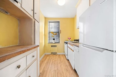 Kitchen with white appliances, white cabinets, light wood-style floors, butcher block countertops, and radiator