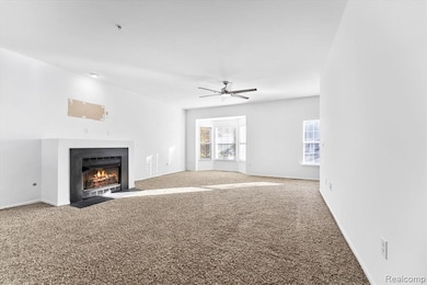 Unfurnished living room featuring carpet floors, a fireplace with flush hearth, and ceiling fan