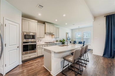 Kitchen featuring decorative backsplash, a kitchen breakfast bar, appliances with stainless steel finishes, a center island with sink, and dark wood-type flooring