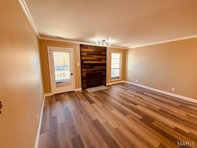 Unfurnished living room with crown molding, wood finished floors, and a large fireplace