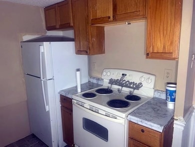 Kitchen with white range with electric stovetop, brown cabinetry, and light countertops