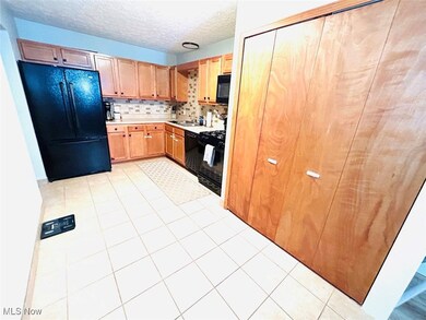 Kitchen featuring light countertops, decorative backsplash, black appliances, light tile patterned floors, and a textured ceiling