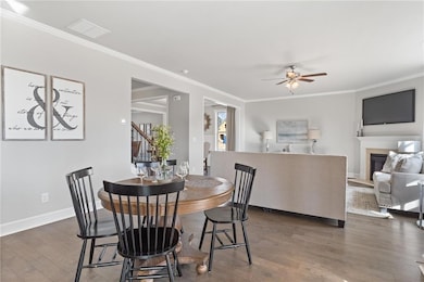 Dining room with baseboards, ornamental molding, wood finished floors, a ceiling fan, and a glass covered fireplace