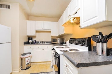Kitchen featuring range with electric stovetop, freestanding refrigerator, dark countertops, under cabinet range hood, and white cabinetry