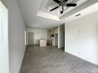 Unfurnished living room featuring a ceiling fan, a raised ceiling, and light wood-type flooring
