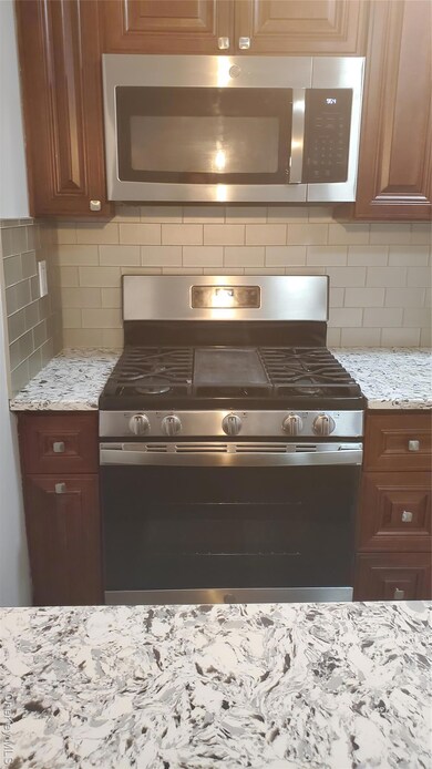 Kitchen with appliances with stainless steel finishes, backsplash, and light stone countertops