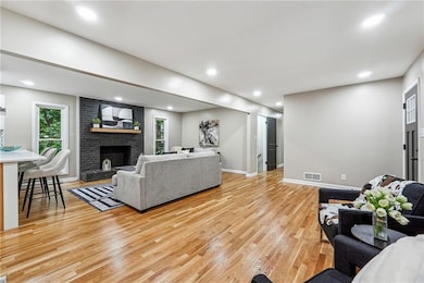 Living room featuring light wood-type flooring, a fireplace, baseboards, and recessed lighting