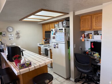 Kitchen with a textured ceiling, brown cabinetry, white appliances, light tile patterned floors, and a breakfast bar