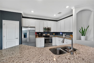 Kitchen featuring appliances with stainless steel finishes, white cabinets, light stone counters, crown molding, and recessed lighting