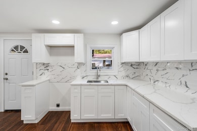 Kitchen with white cabinetry, light stone countertops, dark wood-type flooring, backsplash, and recessed lighting