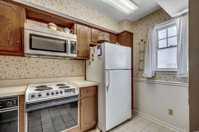 Kitchen featuring stainless steel microwave, freestanding refrigerator, electric range oven, wallpapered walls, and light tile patterned floors
