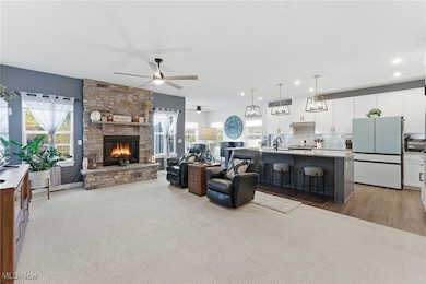 Living area with a stone fireplace, plenty of natural light, ceiling fan, and light wood-style flooring