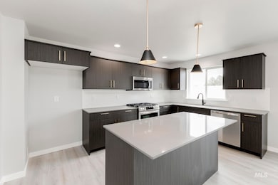 Kitchen with backsplash, stainless steel appliances, pendant lighting, light wood-style flooring, and a kitchen island