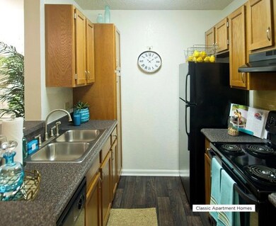 Kitchen featuring black appliances, dark wood finished floors, under cabinet range hood, a textured ceiling, and brown cabinets