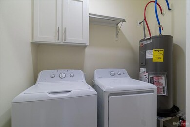 Washroom with electric water heater, cabinet space, and washer and clothes dryer