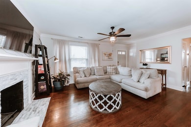 Living room with ceiling fan, dark wood finished floors, a fireplace with flush hearth, ornamental molding, and baseboards