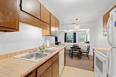 Kitchen featuring white appliances, light countertops, light colored carpet, ceiling fan, and brown cabinets